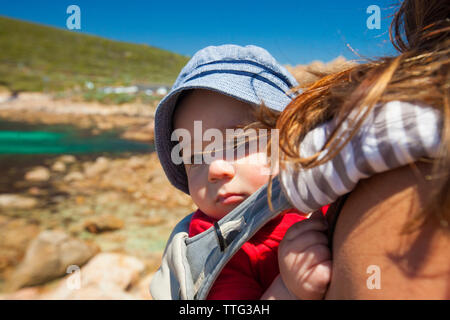 Mittelteil der Mutter mit Sohn bei der Beförderung im Stehen am Strand gegen blauen Himmel Stockfoto