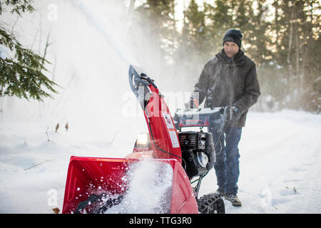 Active Senior Mann mit Schneefräse Maschine zu löschen Auffahrt Stockfoto