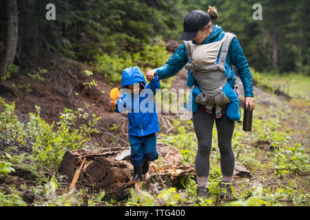 Mutter ihr kleiner Sohn Balance auf einem Baumstamm beim Wandern im Wald zu helfen Stockfoto