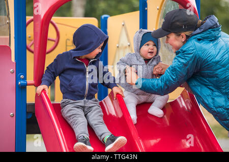 Mutter und Tochter auf dem Spielplatz Rutsche mit älteren Bruder Stockfoto