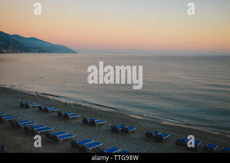 Reihen von leeren blauen Liegestühlen am Strand bei Sonnenuntergang mit Möwen Stockfoto