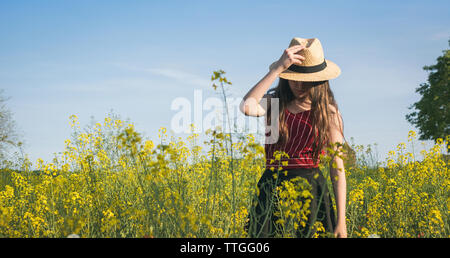 Teenage Mädchen mit Hut stehend auf dem Feld gegen den blauen Himmel während der sonnigen Tag Stockfoto