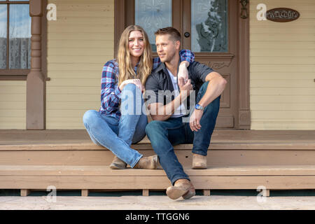 Western Wear junges Paar sitzen auf der Veranda der Ranch House Stockfoto