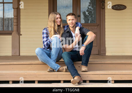 Western Wear junges Paar sitzen auf der Veranda der Ranch House Stockfoto