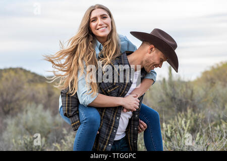 Western Wear junges Paar, Huckepack Fahrt auf der Ranch Stockfoto