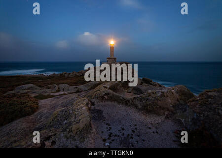 Beleuchtete Punta Nariga Leuchtturm an der Küste gegen Himmel und Meer während der Dämmerung Stockfoto