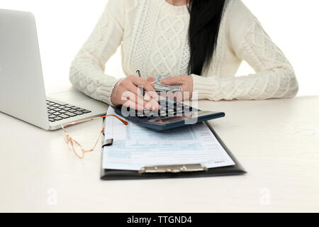 Dunkelhaarige Frau beiseite computer Geldhaltung und Berechnungen, die auf der Weißen hölzernen Tisch, in der Nähe Stockfoto