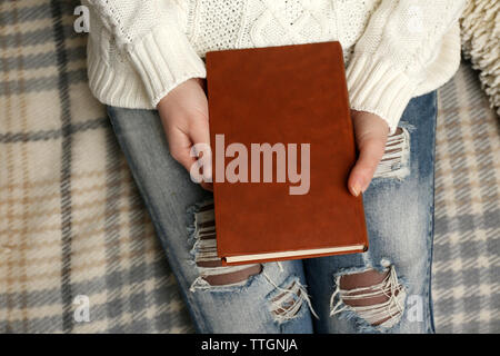 Junge Frau auf dem Sofa sitzen mit karierten Decke abgedeckt und halten ein braunes Buch Cover, in der Nähe Stockfoto