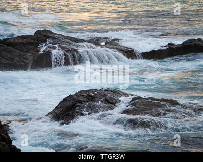 Wasser floss und verschüttete sich über Felsen von Wellen in Strandnähe Stockfoto