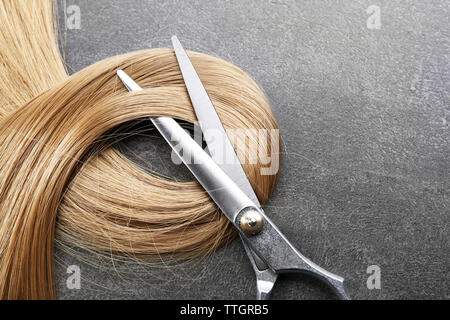 Friseur Schere mit Strang der blonde Haare auf grauem Hintergrund Stockfoto