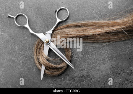 Friseur Schere mit Strang der braune Haare auf grauem Hintergrund Stockfoto