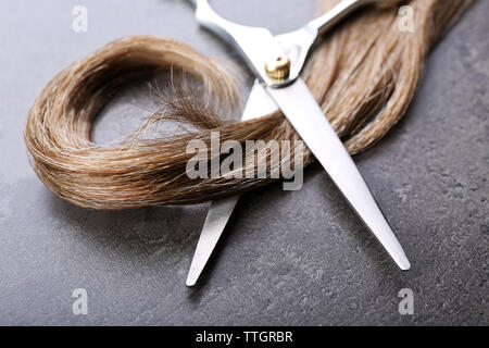 Friseur Schere mit Strang der braune Haare auf grauem Hintergrund Stockfoto