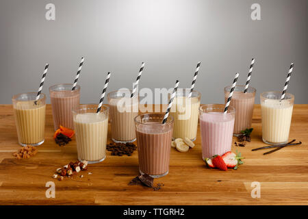 Gläser für die verschiedenen Arten von bunten Milchshake mit Papier Trinkhalme und Zutaten auf einem hölzernen Tischplatte Stockfoto