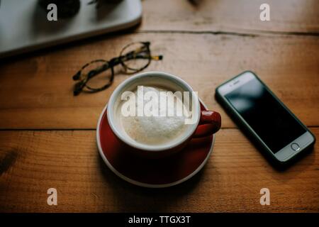 Kaffee Telefon und Gläser auf dem Tisch in einem Cafe mit Fenster Licht Stockfoto