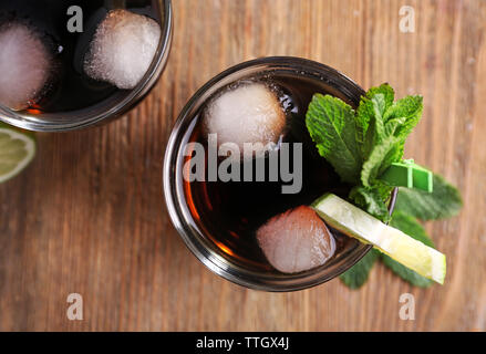 Zwei Gläser Cola mit Eis, Minze und Limette auf Holztisch, Hintergrund, Ansicht von oben Stockfoto