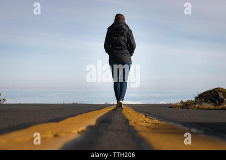 Frau zu Fuß auf der Linie hinunter die Straße über den Wolken am Haleakala National Park auf der hawaiianischen Insel Maui, USA Stockfoto