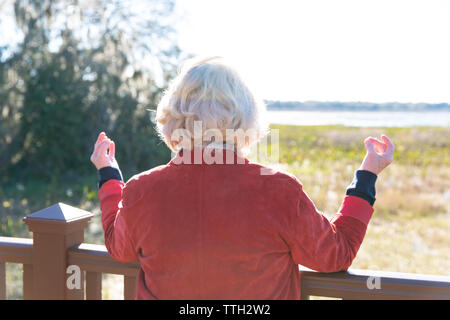 Eine ältere Frau in den 70er Jahren mit Blick auf einen See und meditiert. Stockfoto