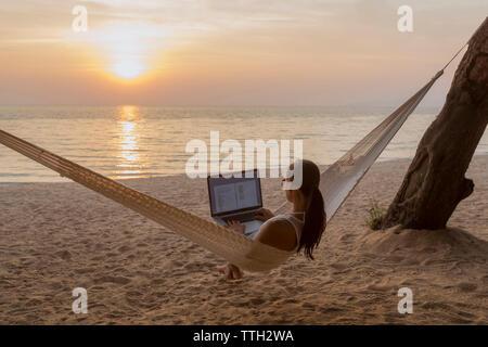 Frau mit Laptop-Computer sitzend auf Hängematte am Strand Stockfoto