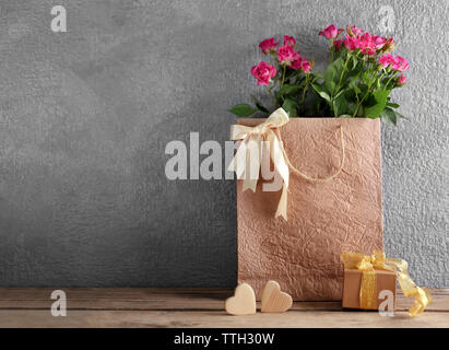 Rosa Rosen in Papiertüte auf hölzernen Tisch gegen die graue Wand, in der Nähe Stockfoto