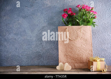 Rosa Rosen in Papiertüte auf hölzernen Tisch gegen die graue Wand, in der Nähe Stockfoto
