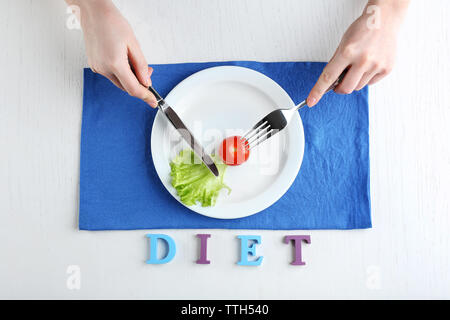 Weibliche Hände, die Messer und Gabel auf Platte mit Cherry Tomaten und Kopfsalat Blatt in der Nähe, Ansicht von oben Stockfoto