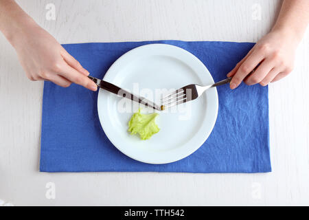 Weibliche Hände, die Messer und Gabel auf Platte mit Stück Salatblatt und single Erbse, Ansicht von oben Stockfoto