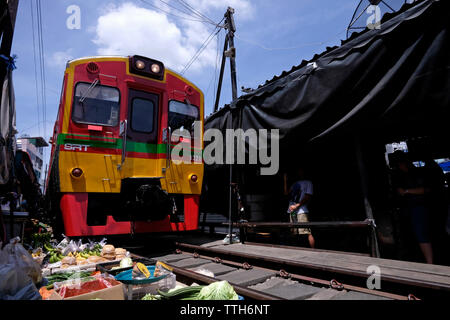 Ein Zug der State Railway of Thailand (SRT), der den Maeklong Railway Market durchquert, auch bekannt als der „Schirm Pulldown Market“ oder Talat Rom Hup., wo Händler ihre Stände und einziehbaren Markisen schnell anpassen, um den Zug passieren zu lassen, und dann schnell wieder Geschäfte aufnehmen, als ob nichts passiert wäre. Der Zug befindet sich in Samut Songkhram, etwa 37 Meilen westlich von Bangkok, Thailand Stockfoto