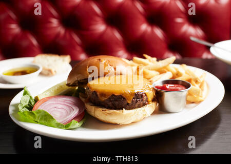 In der Nähe von Cheeseburger mit Pommes Frites auf Teller am Tisch Stockfoto