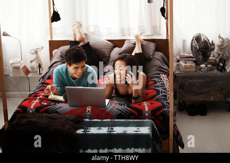 Glückliches Paar mit Laptop auf dem Himmelbett zu Hause Stockfoto