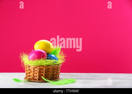 Bunte Ostereier in wicker Nest auf rosa Hintergrund Stockfoto