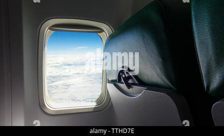 Flugzeugsitz und Windows am Flugzeug. Blick auf den blauen Himmel und Wolken aus dem Flugzeug Fenster Beifahrerseite. Schöne weiße Wolke als durch das Fenster gesehen Stockfoto