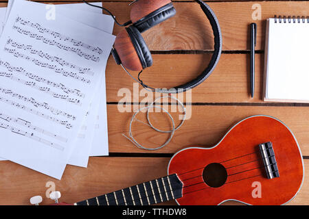 Kleine Gitarre, Kopfhörer und Musik Blätter auf Holz- Oberfläche, Ansicht von oben Stockfoto