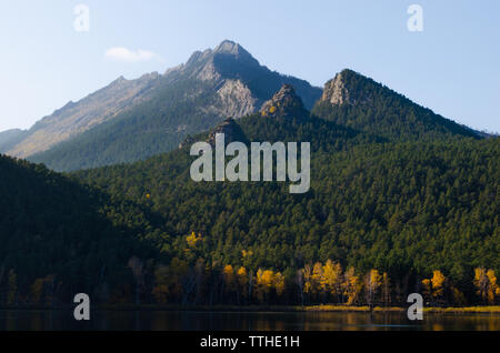 See im Hintergrund der hohe Berge mit herbstlichen Birken und Kiefern bedeckt. Stockfoto