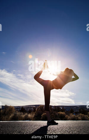 Sportliche frau yoga auf der Straße gegen Himmel während der sonnigen Tag Stockfoto