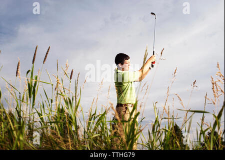 Seitenansicht des männlichen Golfspieler schwingen Golf Club auf Feld gegen Sky Stockfoto