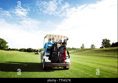 Ansicht der Rückseite des Freunde Reiten in Golfkarre im Feld gegen Sky Stockfoto