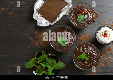 Glas Tassen Schokolade Dessert mit frischer Minze und aufgeschäumter Milch auf schwarzen Holztisch Stockfoto