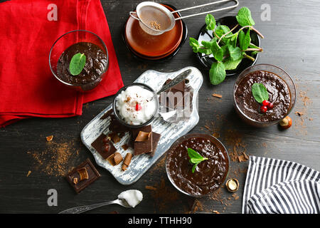 Glas Tassen Schokolade Dessert mit frischer Minze und aufgeschäumter Milch auf schwarzen Holztisch Stockfoto