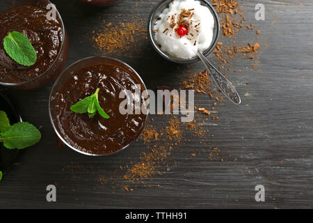 Glas Tassen Schokolade Dessert mit frischer Minze und aufgeschäumter Milch auf schwarzen Holztisch Stockfoto
