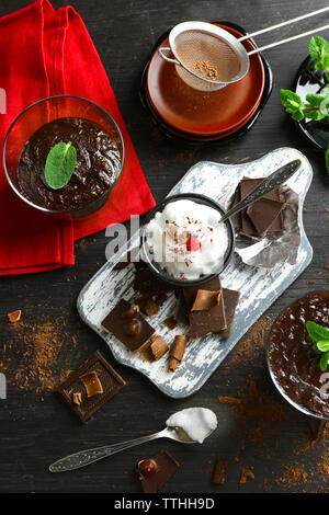 Glas Tassen Schokoladencreme mit frischer Minze und aufgeschäumter Milch auf schwarzen Holztisch Stockfoto
