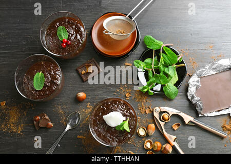 Glas Tassen Schokolade Dessert mit frischer Minze und aufgeschäumter Milch auf schwarzen Holztisch Stockfoto