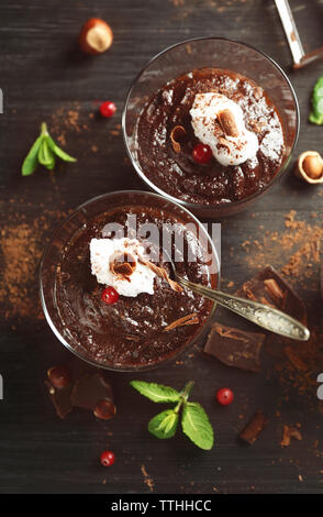 Glas Tassen Schokolade Dessert mit Preiselbeeren, frischer Minze und aufgeschäumter Milch auf schwarzen Holztisch Stockfoto