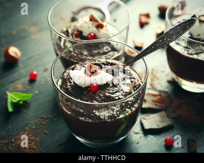 Glas Tassen Schokolade Dessert mit aufgeschäumter Milch und Preiselbeeren auf schwarzen Holztisch Stockfoto
