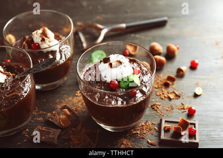 Glas Tassen Schokolade Dessert mit Preiselbeeren, frischer Minze und aufgeschäumter Milch auf schwarzen Holztisch Stockfoto