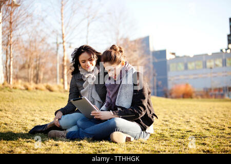 Weibliche Freunde mit digitalen Tablette auf Wiese Stockfoto