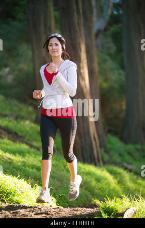 Junge Frau joggen auf Feld gegen Bäume Stockfoto