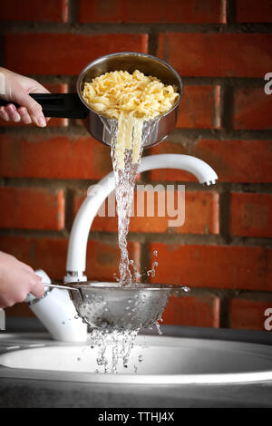 Weibliche Hände gießt Wasser aus gekochten Nudeln über dem Waschbecken in der Küche Stockfoto