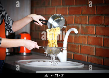 Weibliche Hände gießt Wasser aus gekochten Nudeln über dem Waschbecken in der Küche Stockfoto