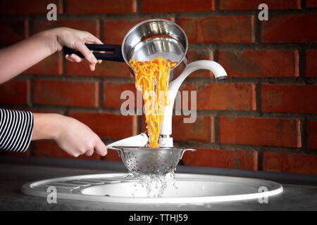 Weibliche Hände gießt Wasser aus gekochten Nudeln über dem Waschbecken in der Küche Stockfoto