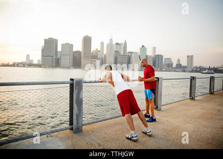 Vater im Gespräch mit Menschen, die auf der Promenade am East River in der Stadt gegen den Himmel Stockfoto